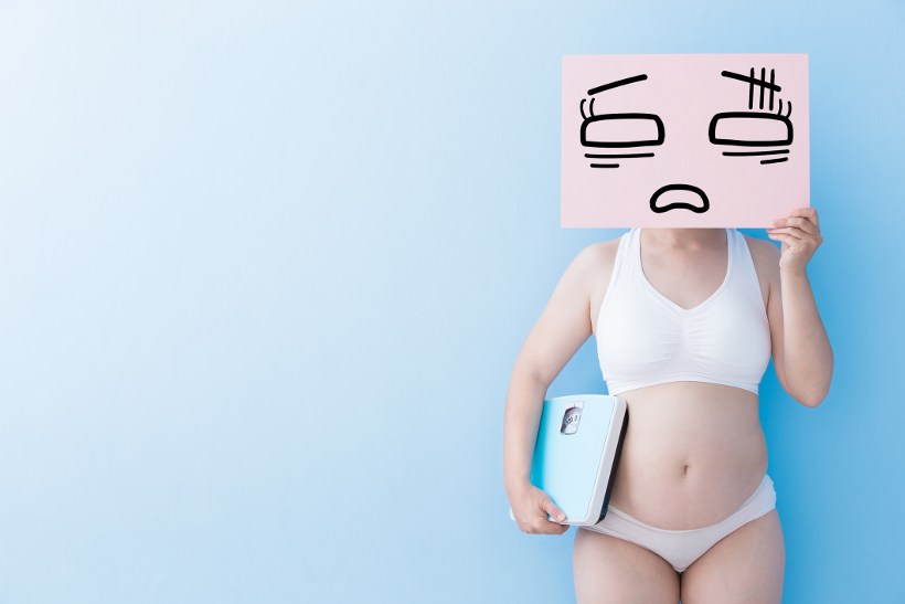 chubby woman holding scale and sign to cover face