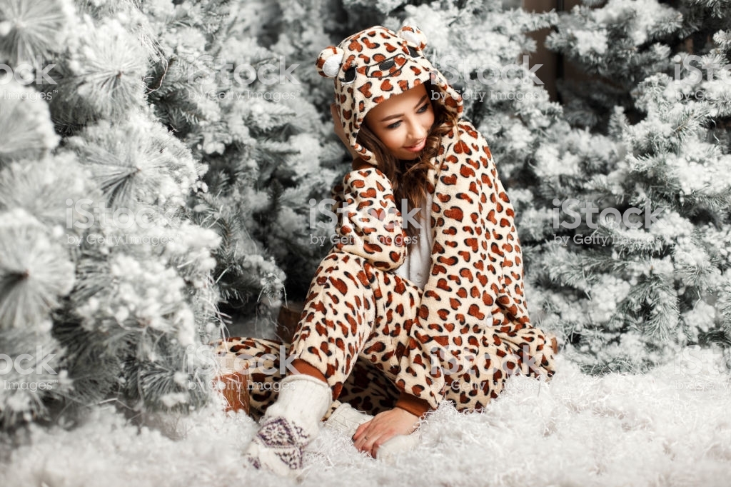 Happy cute girl in a trendy bear pajamas sitting near a Christmas tree